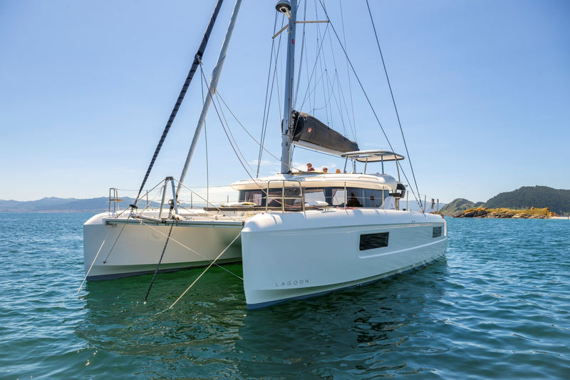 A Lagoon 43 at anchor seen head-on from the water: two white hulls, the flat bridge deck between them, mast and furled sails above.