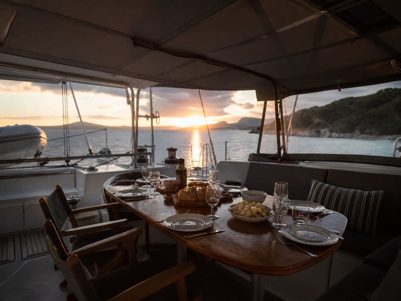 The cockpit table laid for dinner under the bimini, low evening sun coming in over the water.
