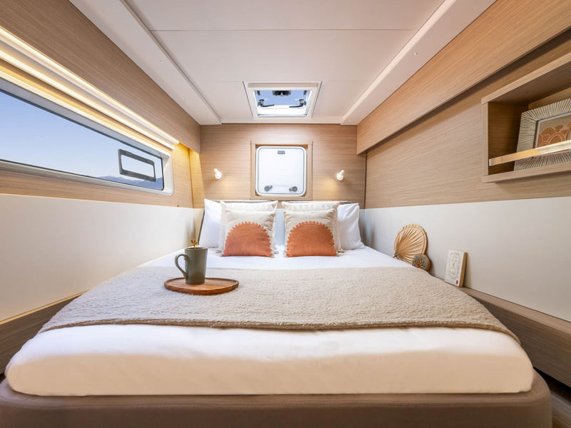 A double guest cabin in the hull: the berth under a long hull window, pale oak lining, a reading shelf above.