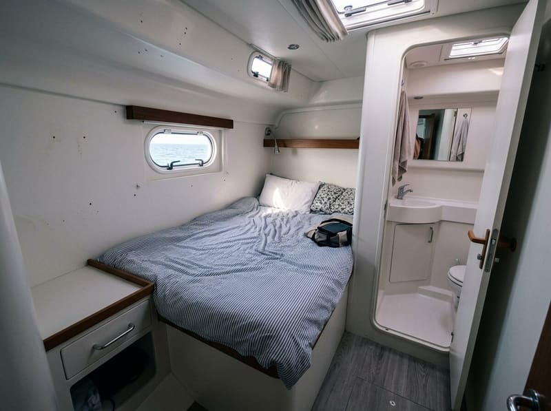 A double guest cabin in the hull, hull window above the berth, the door of its own bathroom standing open.