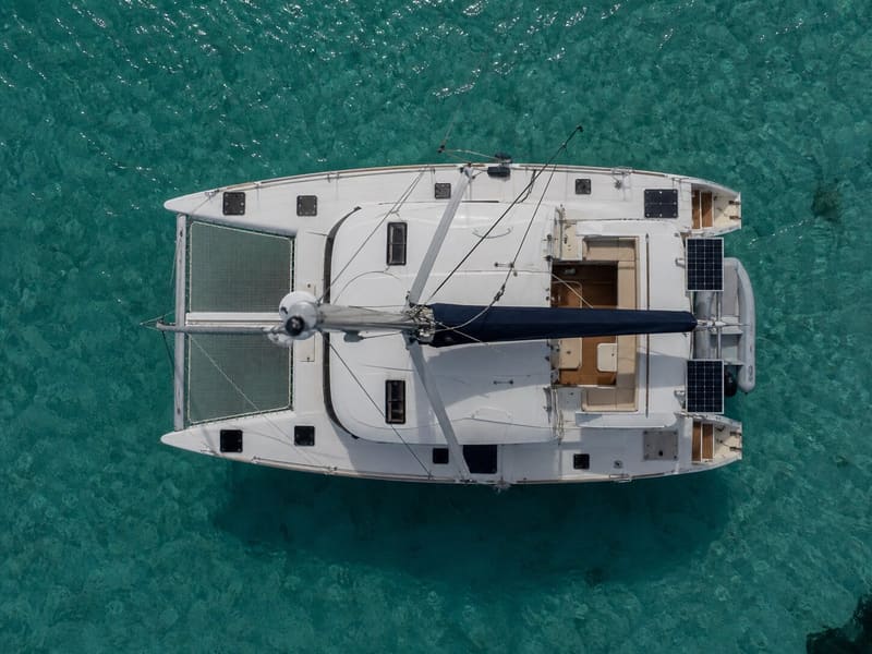A cruising catamaran seen from directly overhead at anchor: both hulls, the trampoline forward, the cockpit aft.