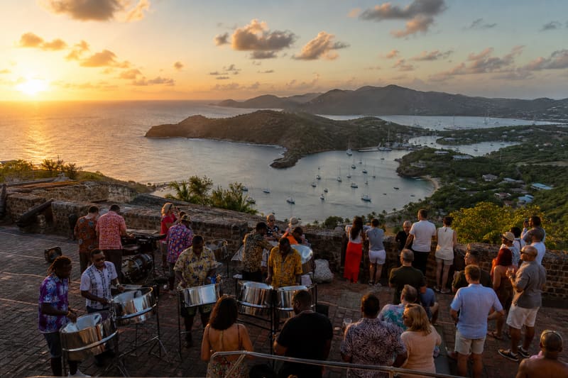 A hilltop fort terrace above a harbour full of anchored yachts at sunset, a band playing on the ramparts.