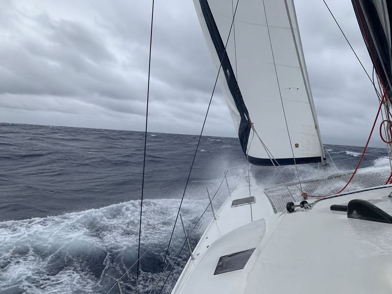 Open ocean from the deck under sail: Atlantic swell running, no land, the boat working.