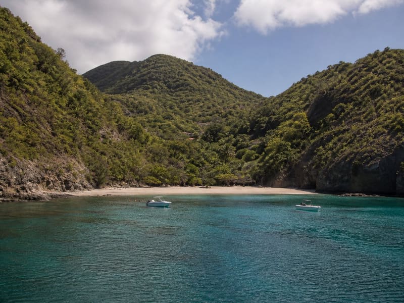 The cove at Pain de Sucre, Les Saintes: pale sand between two green headlands, small boats at anchor.