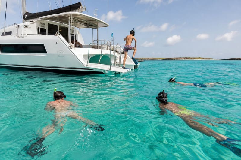 People swimming and snorkelling beside the catamaran at anchor, one of them stepping in off the transom.