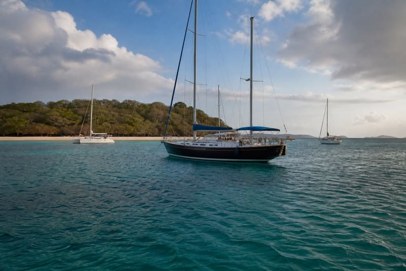 Two or three boats lying to anchor in turquoise water off a small green Grenadines island.