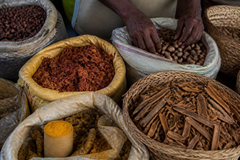 A Grenada market stall of nutmeg, mace, cinnamon bark and cocoa, a vendor’s hands sorting them.