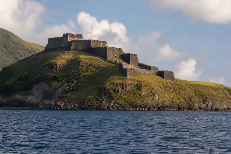 Brimstone Hill Fortress on St Kitts from the sea: dark stone ramparts high on a green headland.