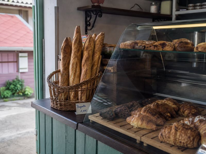 A bakery counter in Les Saintes: baguettes upright in a basket, pastries under glass, a handwritten price card.