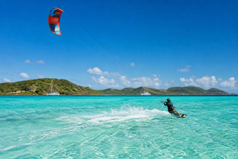 A kitesurfer carving across a shallow turquoise lagoon inside a reef, a bright kite high in a clear sky.
