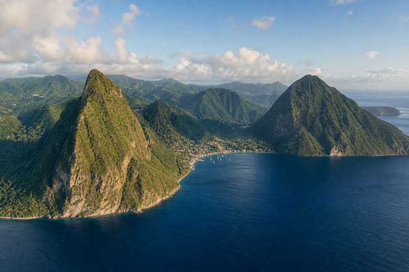 The two Pitons of Saint Lucia from a helicopter: two forested volcanic peaks straight out of the sea, Soufrière and its bay between them.