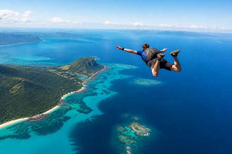A skydiver in freefall above a Caribbean headland, reef and open ocean below.