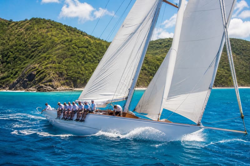 A classic twelve-metre racing yacht heeling under full sail with crew hiking out along the rail.